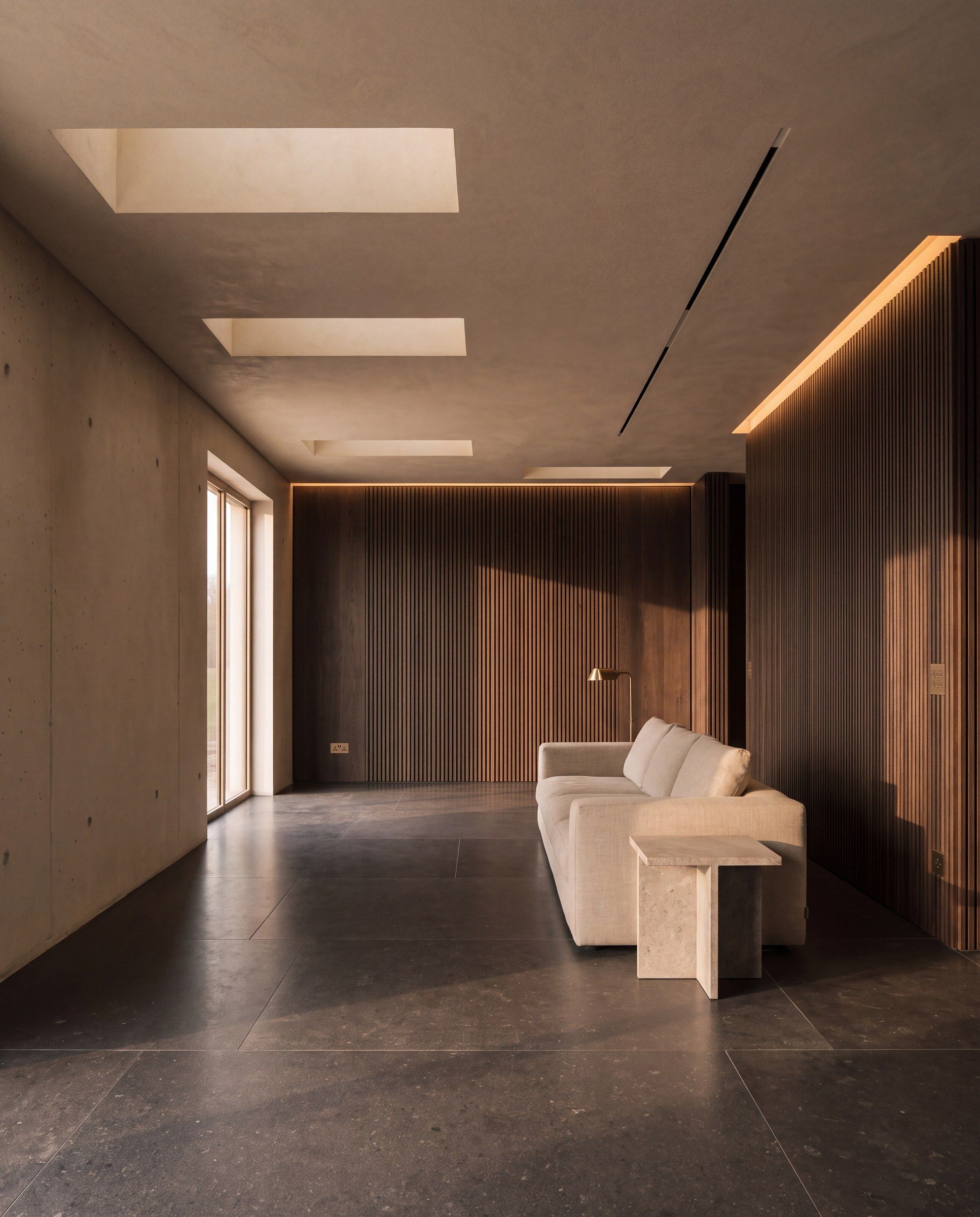 Afgewerkte woonruimte met een wand van walnoten latten, een beige sofa met messing vloerlamp en een travertijnen bijzettafel op een donkere steenvloer